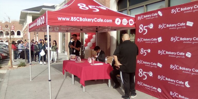 Line of people waiting under a red 85°C Bakery Cafe tent at the grand opening event in Shanghai Plaza, Las Vegas Chinatown.